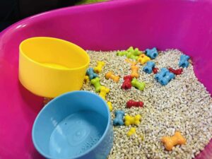 różowa misa z kaszą i kolorowymi elementami – terapia dotykowa, SI